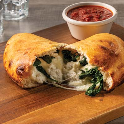 Cheese and spinach calzone cut in half with sauce on the side.